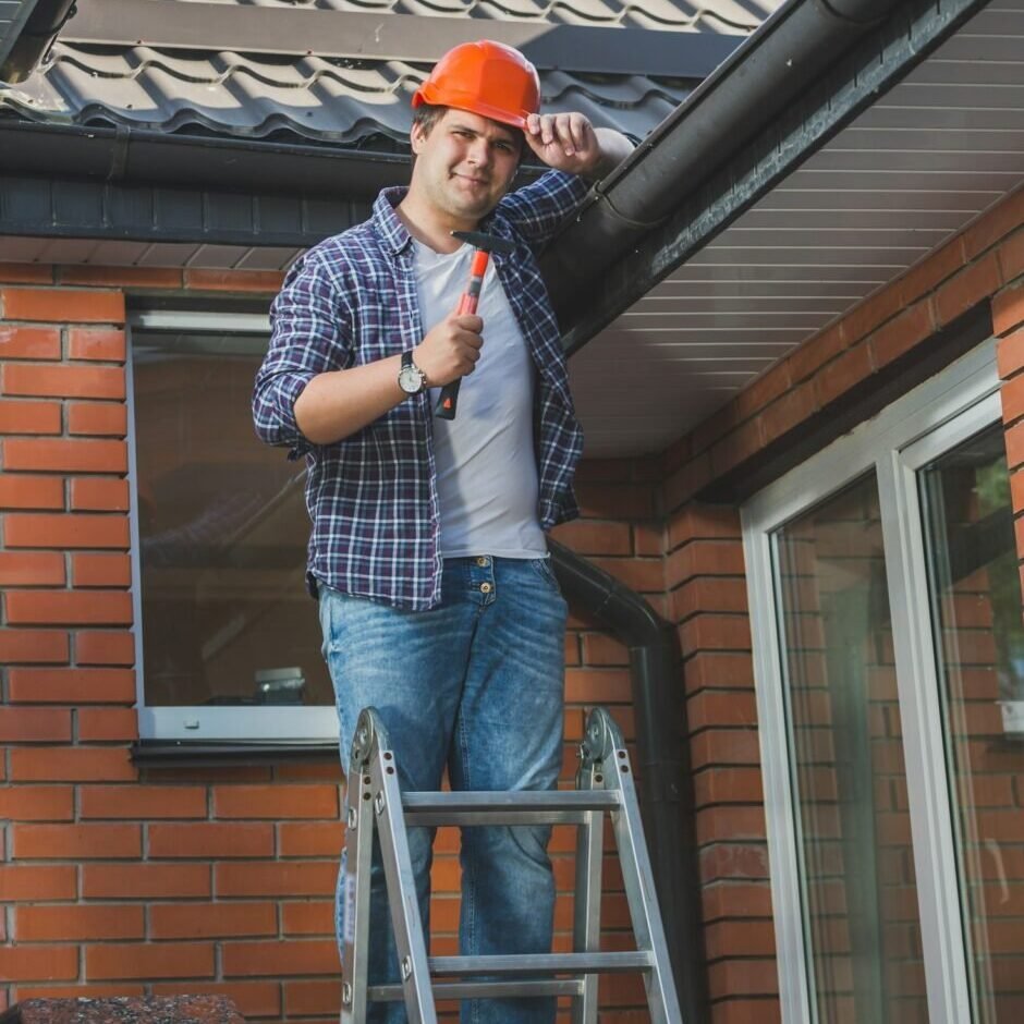 smiling carpenter posing with hammer on step ladder under the roof 1 e1780769632237 tulleycontractingservices.com